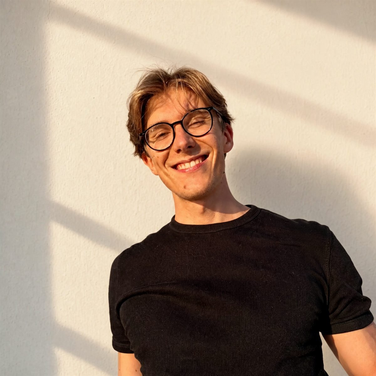 Luis lächelnd vor einer hellen Wand im Abendlicht